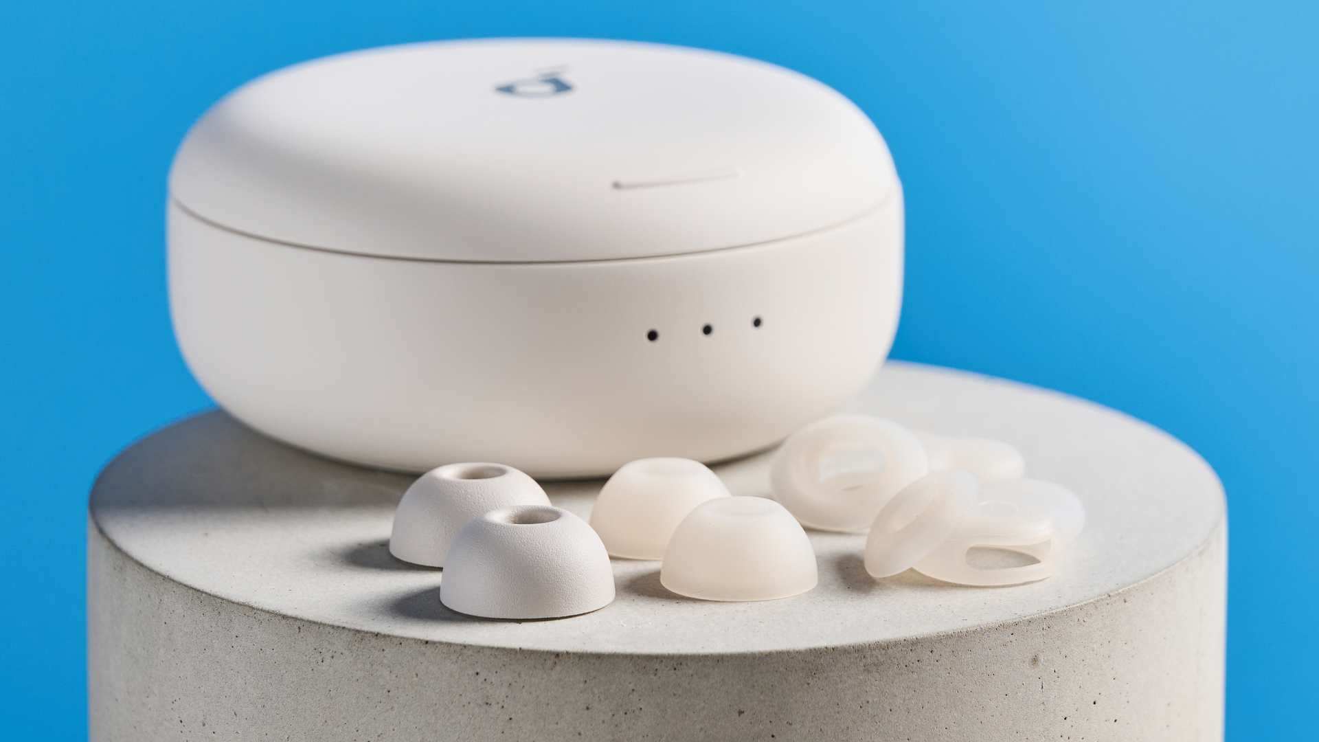 The Soundcore Sleep A30 earbuds spare ear tips and wings on a stone plinth against a blue background