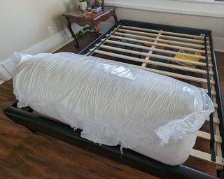 Avocado Green mattress, rolled in plastic wrap at the bottom of bed frame