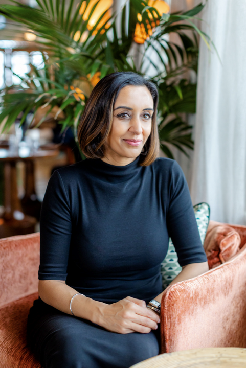 woman in black top on an orange chair with plant in background