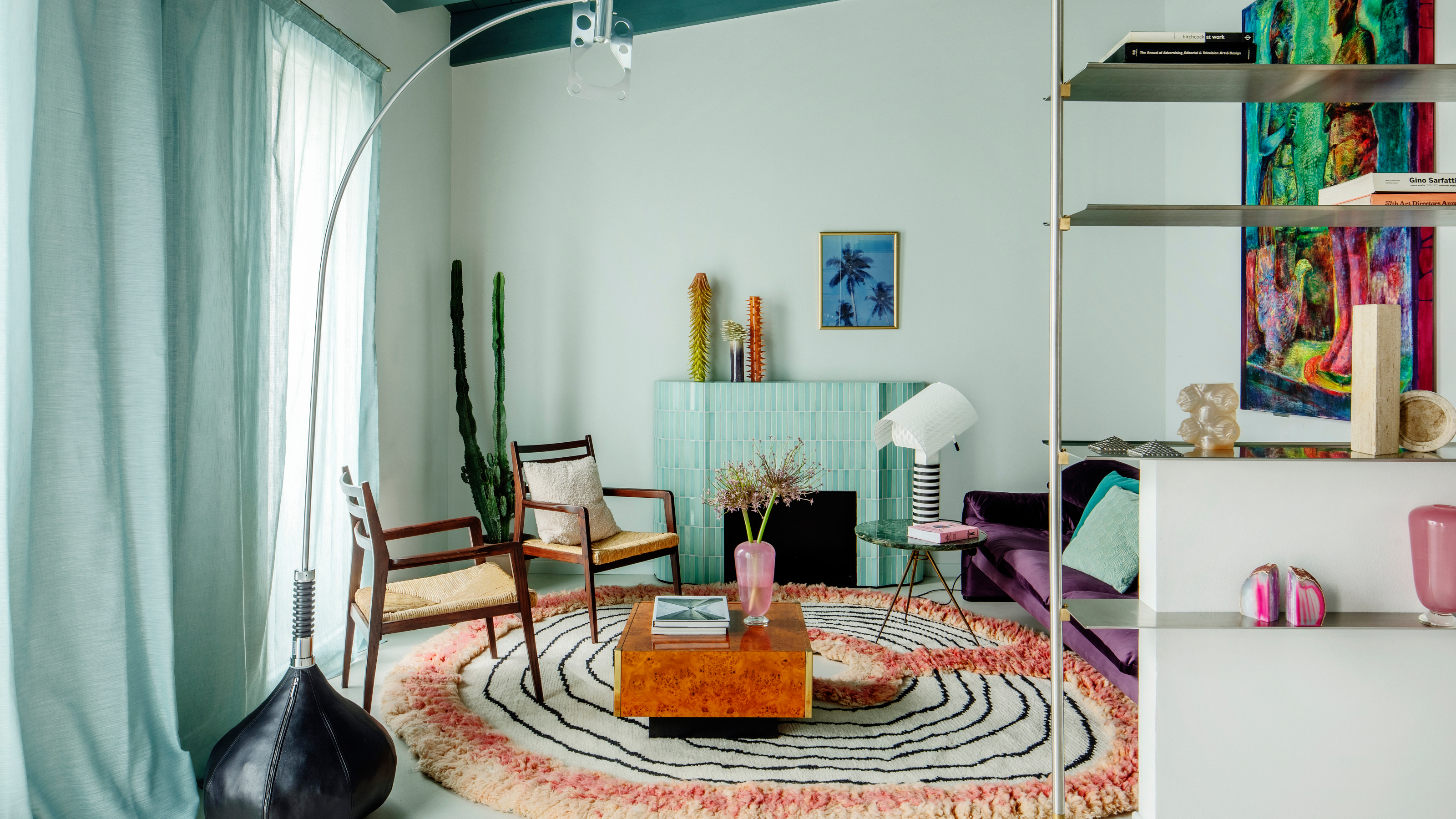 Living room with turquoise ceiling, turquoise tiled fireplace, circular rug and wooden armchairs with burl wood coffee table