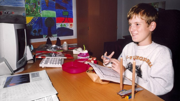 a boy (Mats Steen) sits at his desk in front of a small computer, while holding a pencil in front of an open workbook