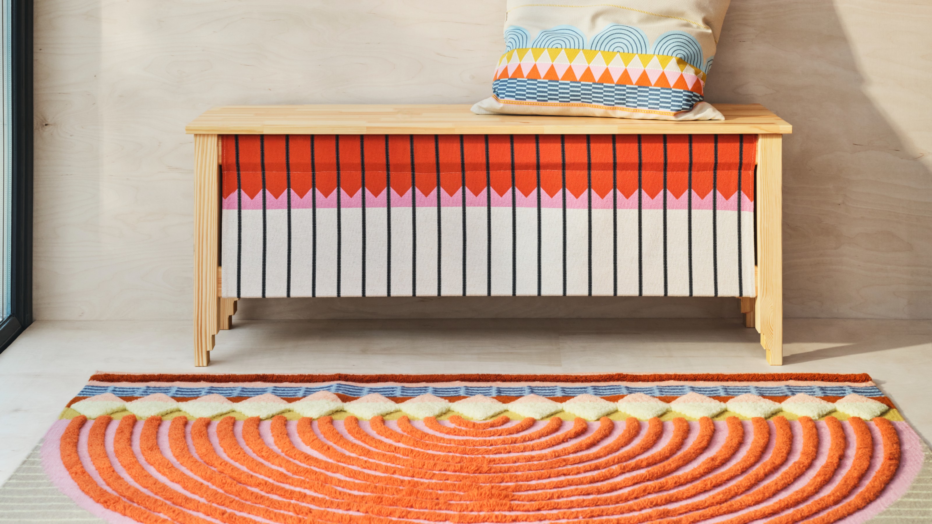 A patterned storage bench with a rug and a cushion from the IKEA OMMJÄNGE collection
