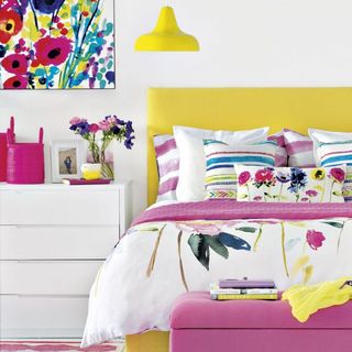 bedroom with white wall yellow bed with pink designed cushion white drawer and yellow lamp