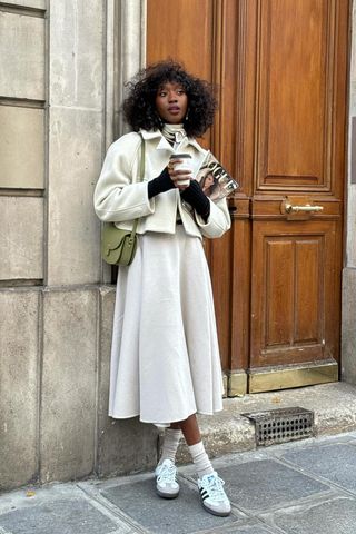 a photo showing shoes to wear with skirts with a woman standing outside wearing a white jacket with a white midi skirt and white sneakers