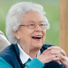 Queen Elizabeth wearing a blue vest and sweater smiling
