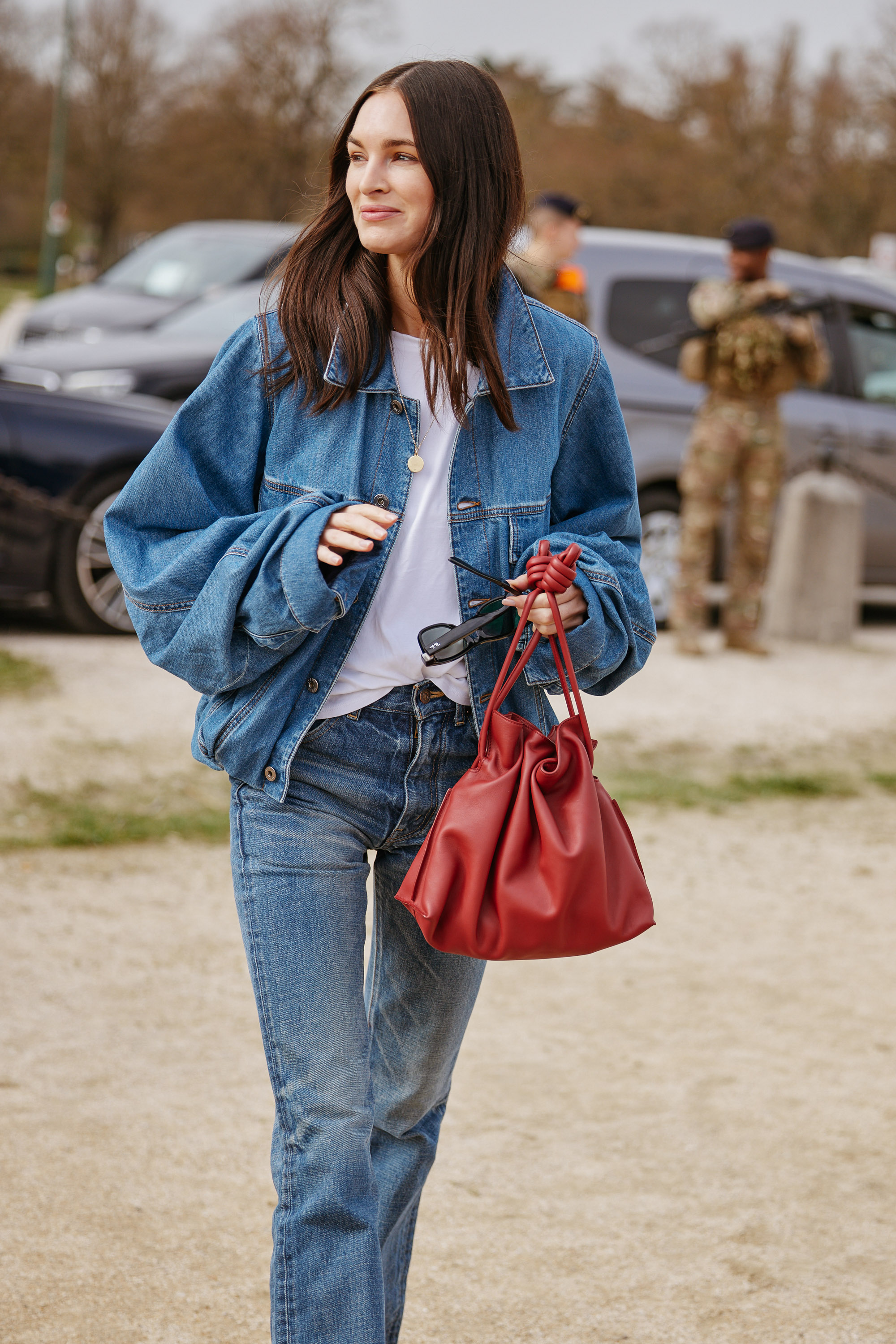 Woman wears denim jacket, white T-shirt, blue jeans and carries red Loewe flamenco bag