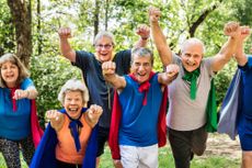 A group of older adults wearing super hero capes with their fists in the air