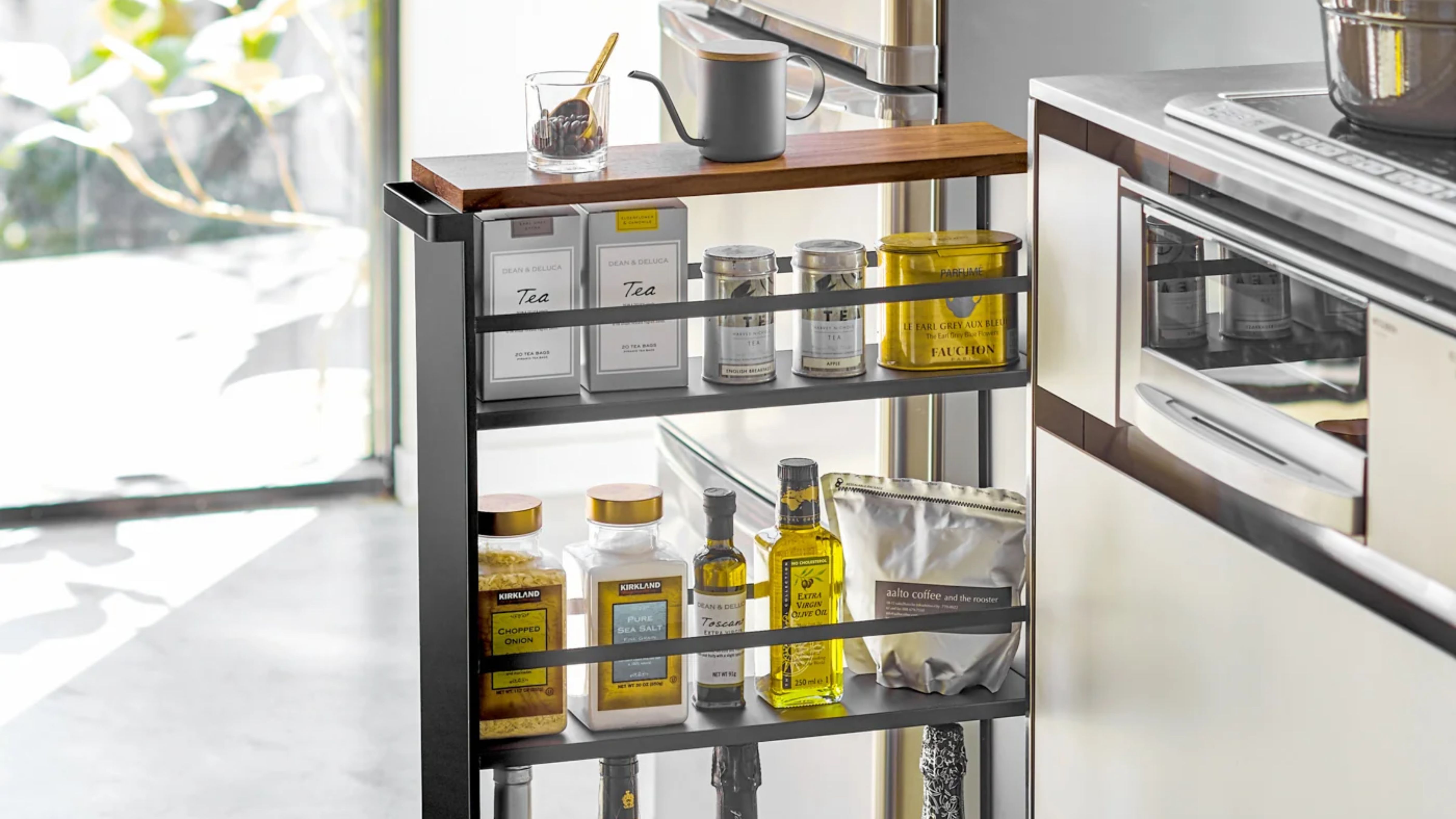 Three-tier rolling storage cart by Yamazaki Home holding assorted cooking essentials inside of a sunlit modern kitchen