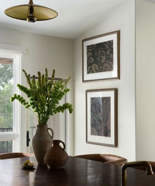 A kitchen corner with two framed abstract artworks on the wall and a jug full of greenery on the edge of the wooden kitchen island