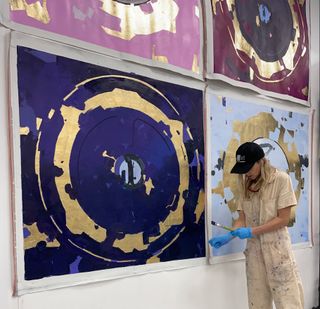 a woman in coveralls stands next to four colorful paintings of a spacecraft hatch