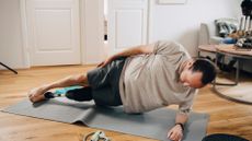 amputee man performing a side plank on a grey exercise mat in a living room setting and wooden floor.