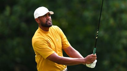 Tony Finau holds his finish on a drive while wearing a yellow top and white cap