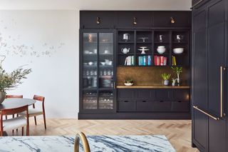 a black kitchen with a glass-fronted unit that has wine storage in. Next to it, a brass effect counter and backsplash sits under open storage with cookbooks and kitchen decor