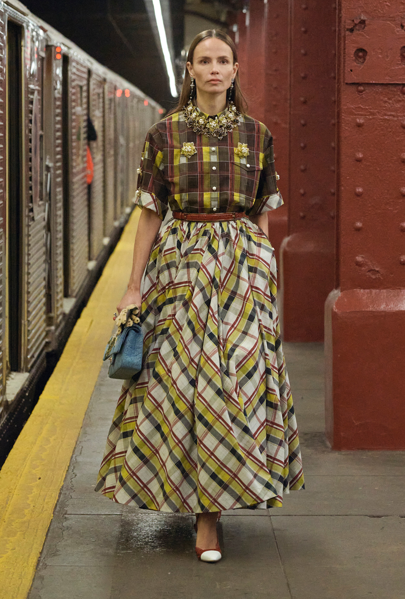 a model wearing a brown, yellow, and white flannel shirt and plaid skirt walking in Chanel's Métiers d'Art 2026 show