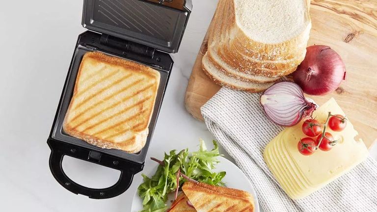 the VonShef Sandwich maker, one of the best sandwich toaster options, with a sandwich inside it, and bread, onions and cheese ingredients on a wooden board