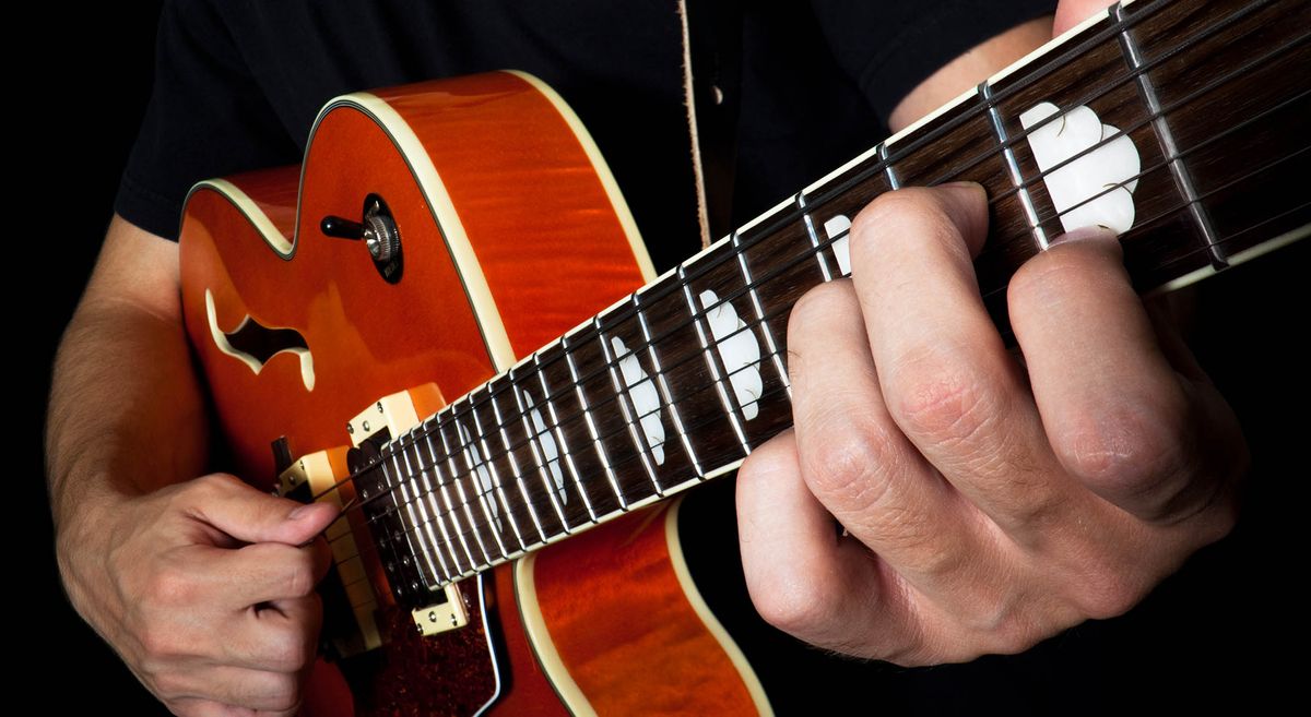 A close-up of a man playing chords on a single-cut Gretsch semi-hollow electric guitar in Round-Up Orange