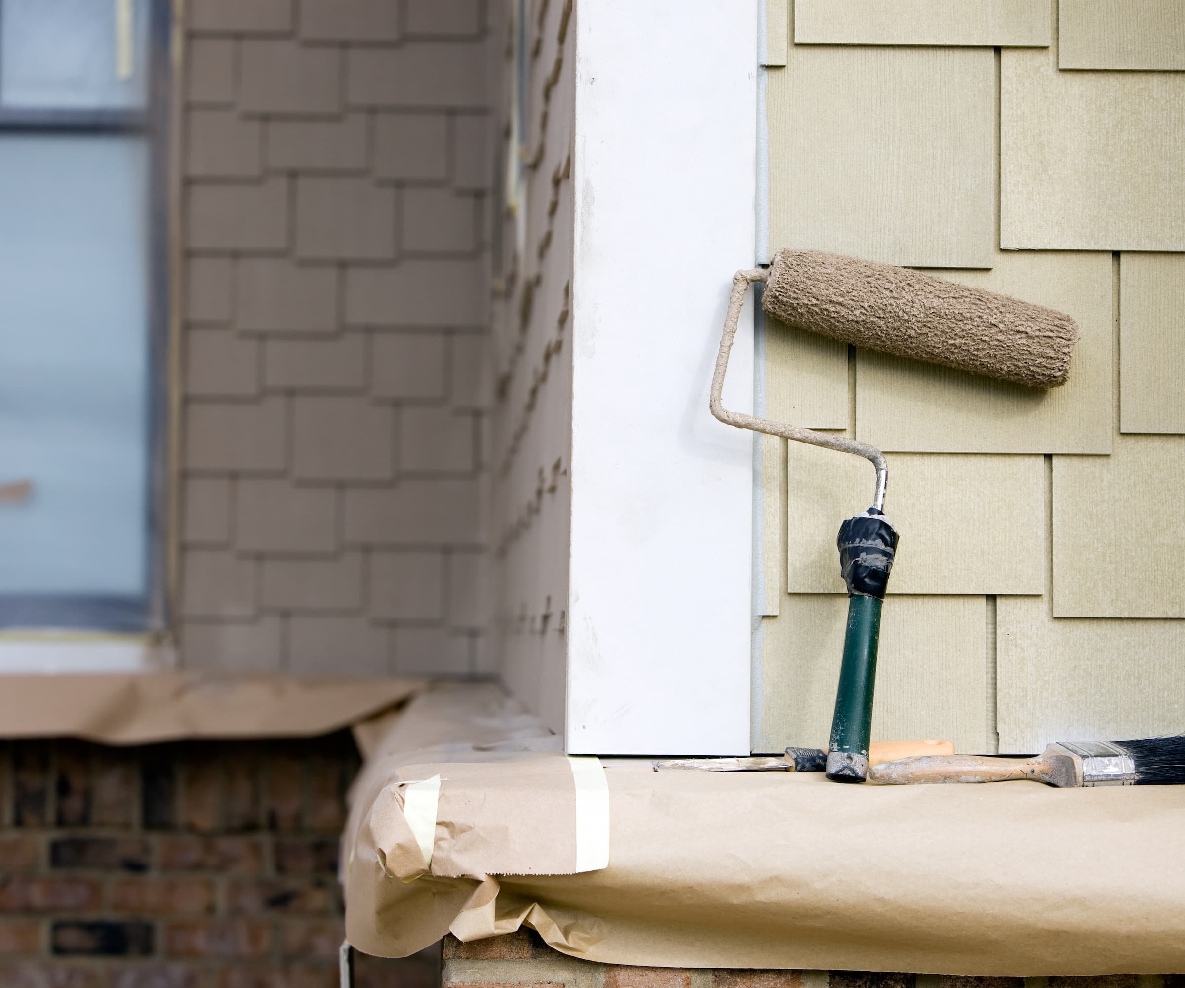 A roller paint brush leaning against the side of a white house