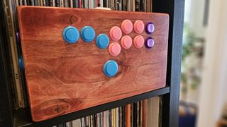 Custom wooden hitbox with bubblegum colored buttons on a bookshelf