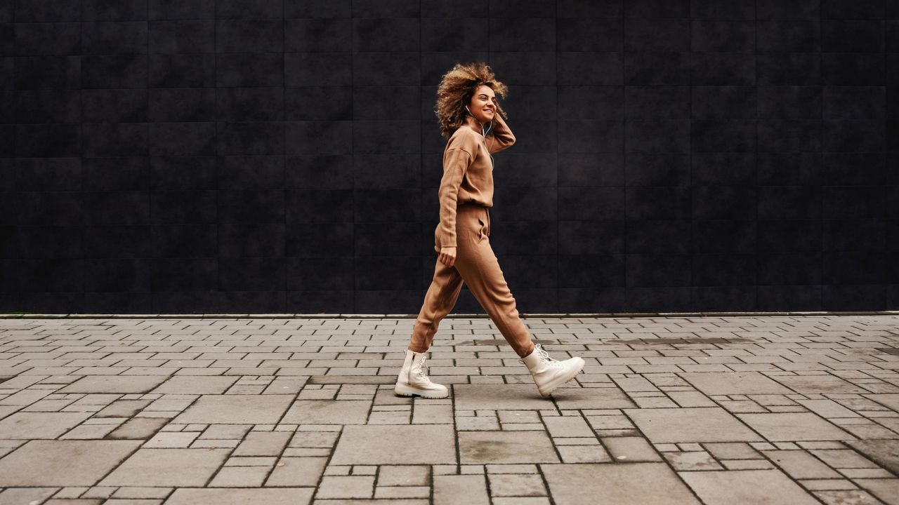 Young fashionable woman with curly hair walking on the street and listening to the music