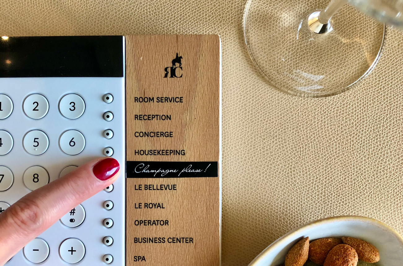 A finger presses a button for Champagne Please in a hotel suite call system