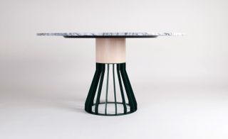 View of the 'MeWoMa' dining table featuring a marble top and light wood and dark green metal base pictured against a light grey background