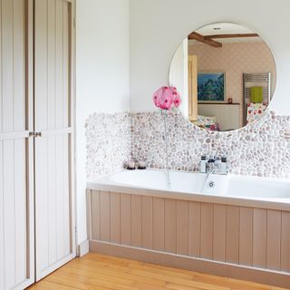 Neutral bathroom with wood panelling stone splash back and round mirror