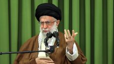 Ayatollah Ali Khamanei speaking in front of a green curtain into a mic