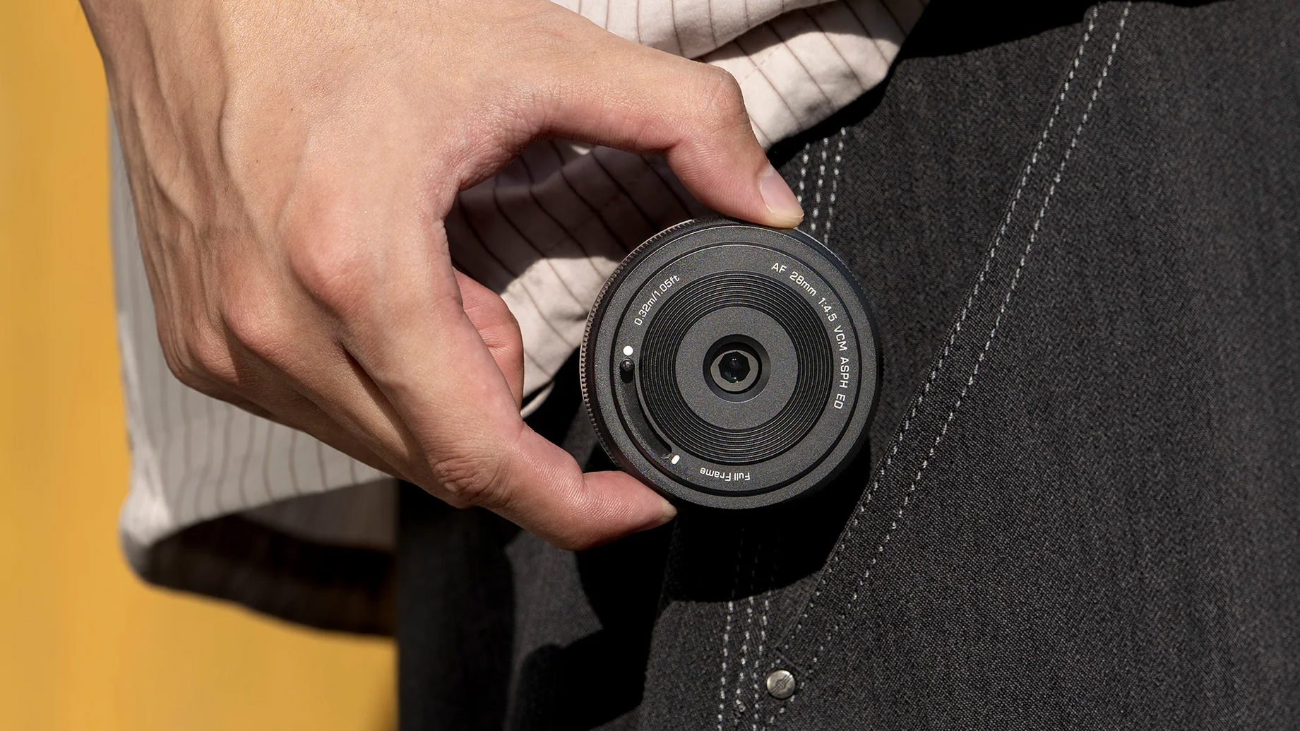 A hand pulling the Viltrox AF 28mm f/4.5 L lens out of a pocket