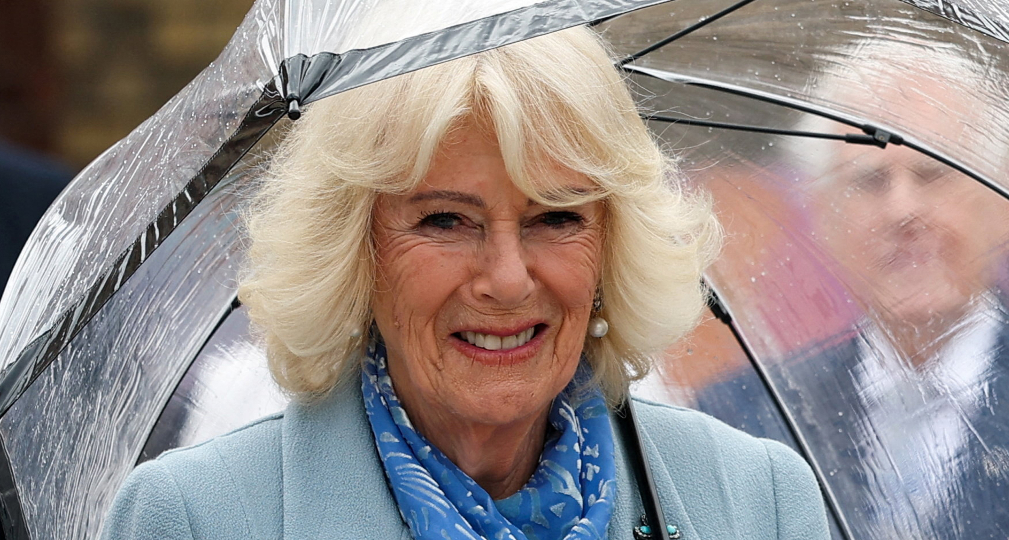 Queen Camilla wearing a blue coat holding an umbrella