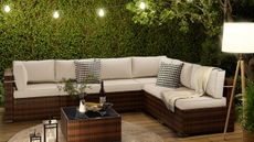 a patio with a large sofa, a small coffee table, string lights, a floor lamp, and a large hedge in the background