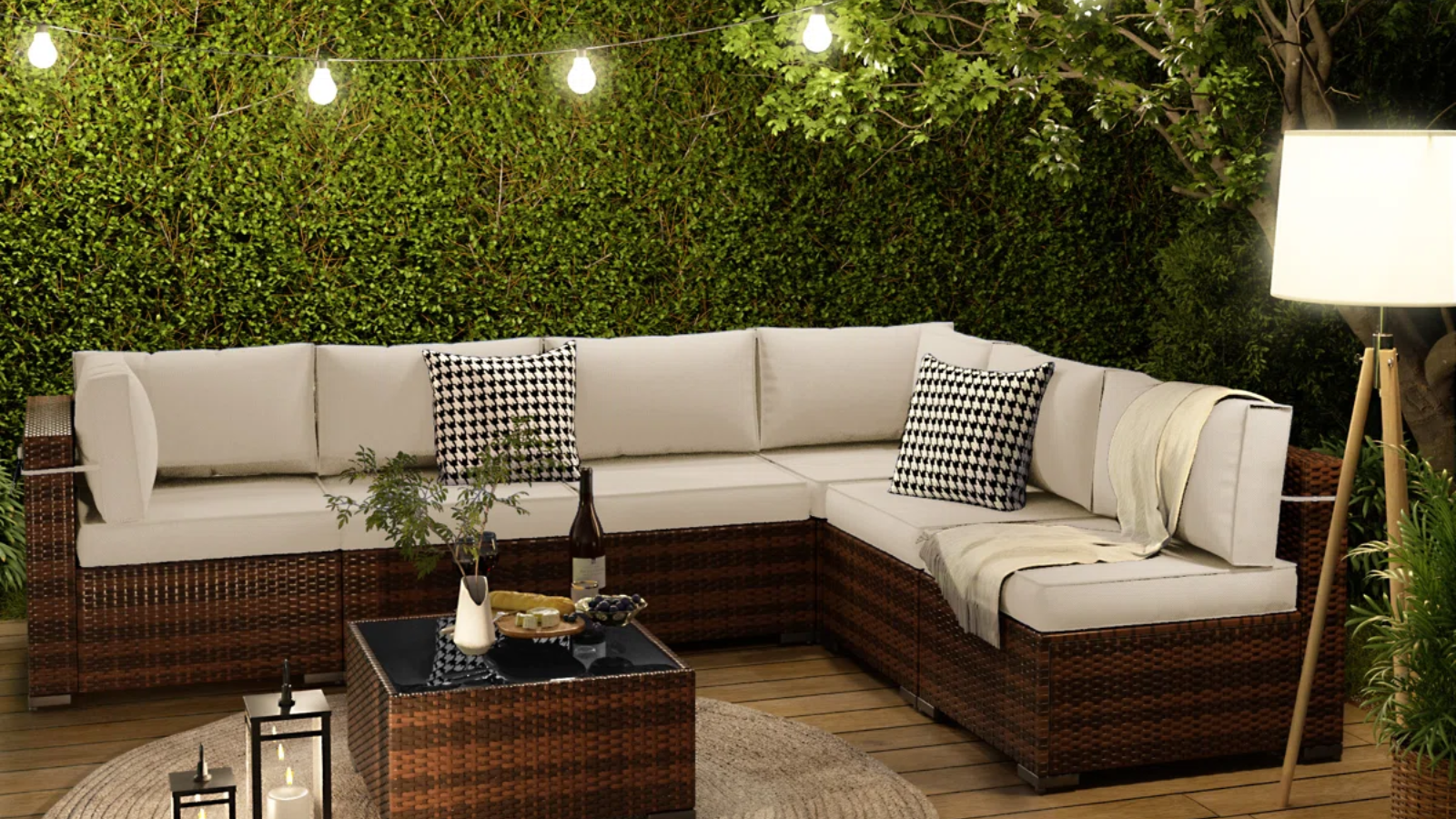 a patio with a large sofa, a small coffee table, string lights, a floor lamp, and a large hedge in the background
