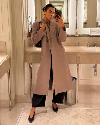 Rochelle Humes wears pointed toe flats, black jeans, a taupe trench coat, and gold earrings.