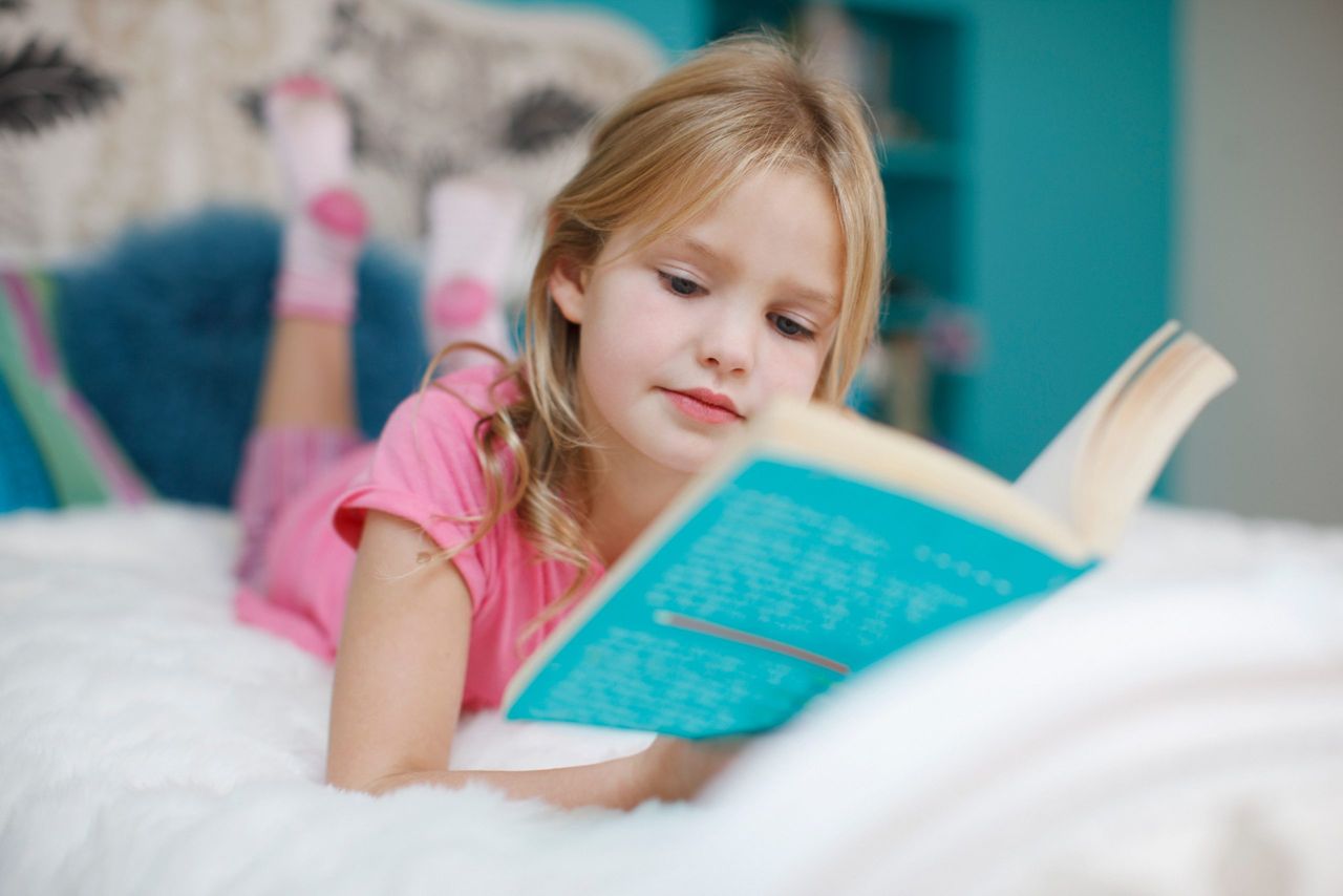 A little girl reading children&#039;s book quotes on her bed.