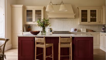 Cream kitchen with a dark red kitchen island and rattan bar stools