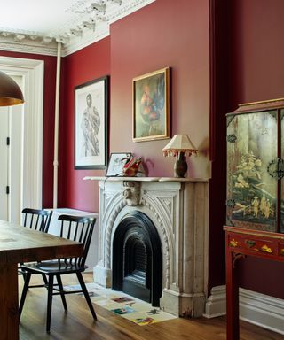 Cream fireplace hearth with hand painted tiles in rust colored room with art on the walls and hardwood floors