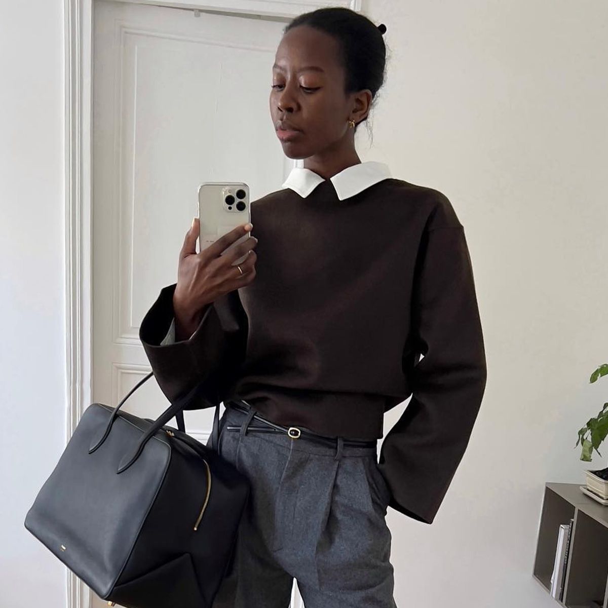 Sylvie Mus holding a structured black duffle bag against tailored gray pants.