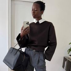 Sylvie Mus holding a structured black duffle bag against tailored gray pants.