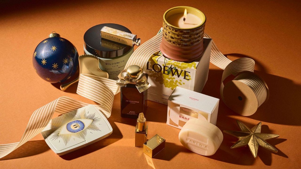 The best luxury beauty gifts for 2024 including Loewe Mimosa candle, Hermes Barenia soap, Tom Ford lip balm, Hourglass Ambient Lighting Edit, Jo Malone London Myrrh &amp; Tonka, Sisley Gua Sha, Wildsmith Bath Salts and Dior Lipstick, intertwined with festive Christmas ribbon