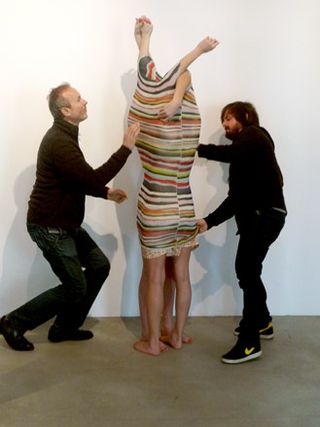 Two people encased inside a striped piece of fabric with their arms appearing out of the top