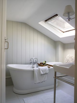 Roll top bath in neutral bathroom with shiplap paneling and velux window