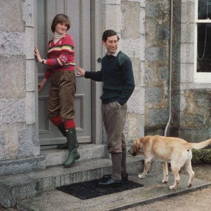 Princess Diana standing in a doorway wearing Hunter boots next to Prince Charles and his dog