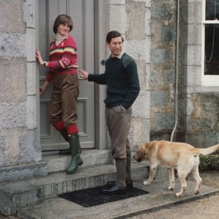 Princess Diana standing in a doorway wearing Hunter boots next to Prince Charles and his dog