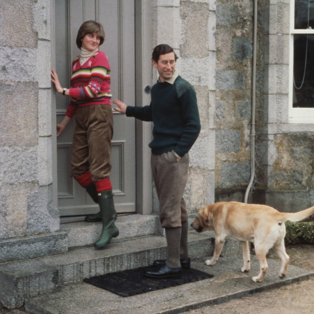 Princess Diana standing in a doorway wearing Hunter boots next to Prince Charles and his dog