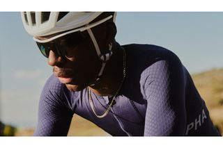 A man in a blue jersey rides at a 45* angle to the camera wearing the Rapha Reis sunglasses