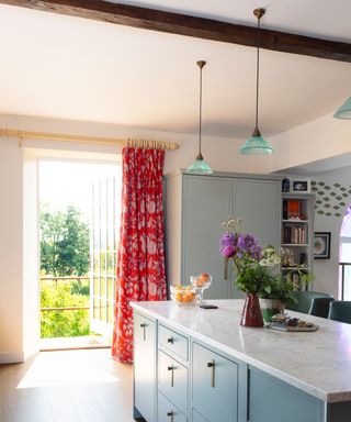 Country kitchen with blue kitchen island, matching cabinetry, blue glass pendant lights, red curtains