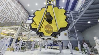 Workers in a clean room moving the James Web Space Telescope with a crane