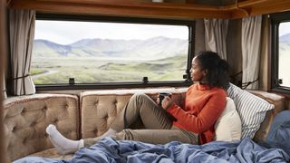 A woman sits in her caravan with tea admiring the mountain view
