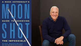 a man in a blue sweater smiles in a chair next to a book cover that reads "moonshot"