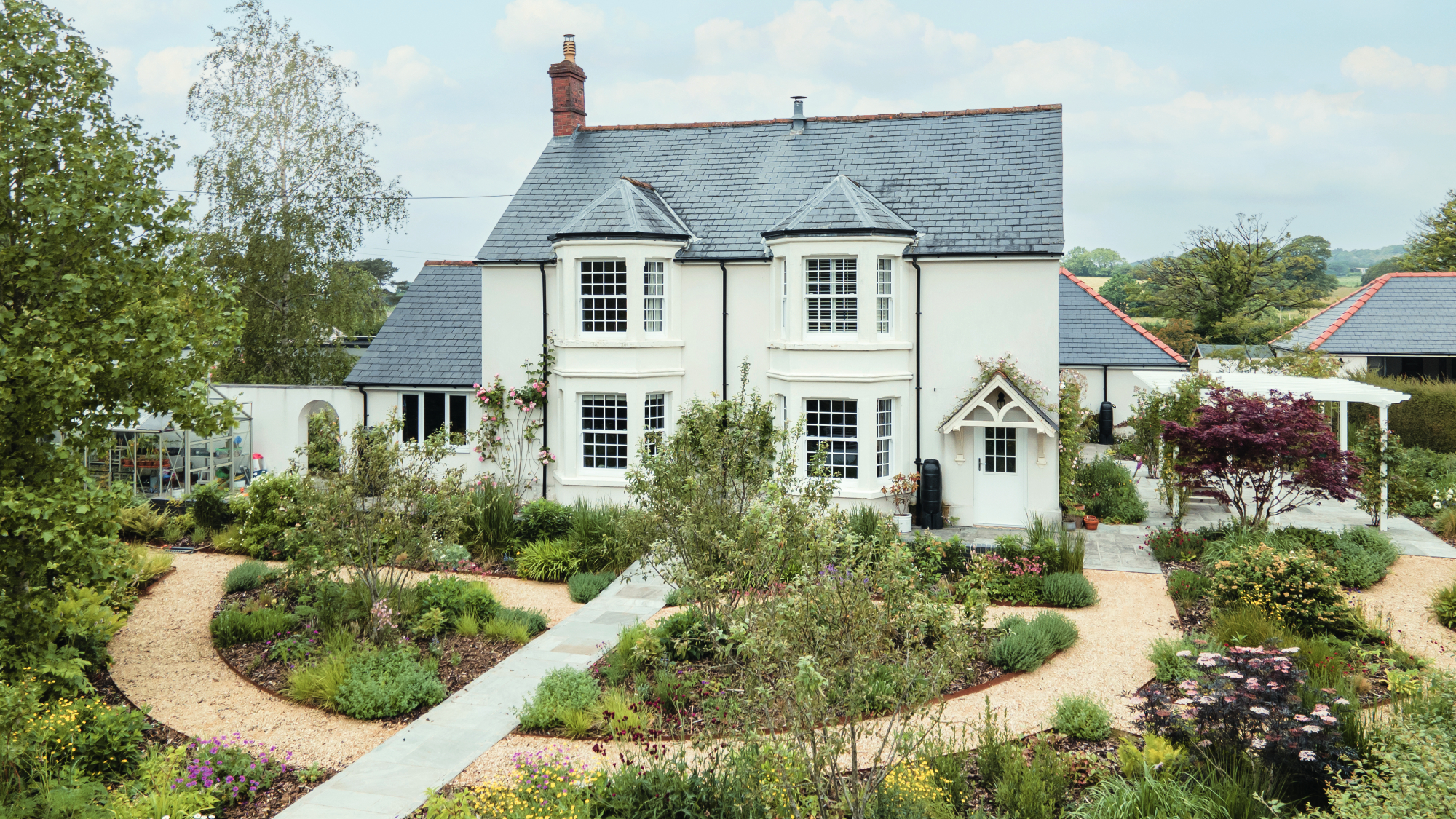 large white house with paved and gravel garden paths and planted areas