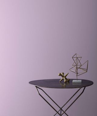 lilac wall with black round table with two decorative gold items